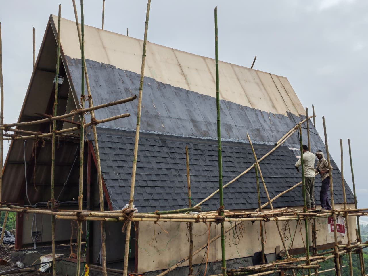 Real construction photograph showing the A-frame cottage exterior during active structural finishing work